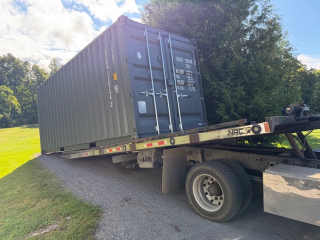 Shipping container being loaded onto a tilt-bed truck