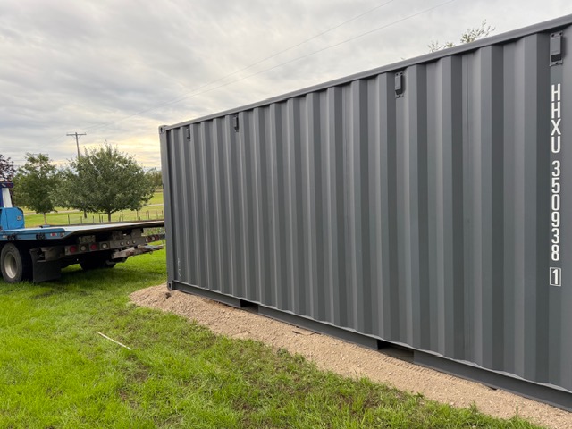 Shipping container set on grass with a trailer nearby